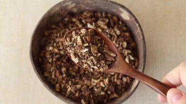 Dried burdock root for making medicinal tea in a wooden spoon on a beige background with a plate