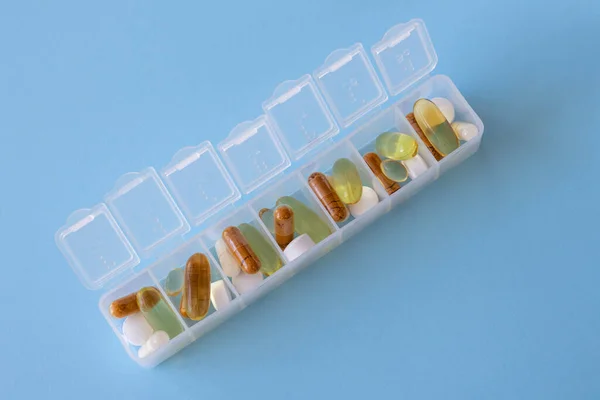 Open organiser with tablets and supplements and vitamins on a blue background. Omega 3, curcumin, magnesium, vitamin D
