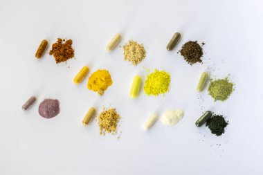 Opened and whole capsules of supplements on white background. Various pills and vitamins. From top right to left as follows: curcumin, vitamin C, ant tree bark, quercetin, q10, vegetable supplement