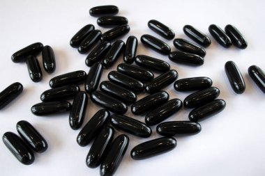 Black Activated Charcoal in capsules on a white background, top view. Treatment of the digestive system and poisoning.