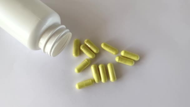 一罐食品补充剂放在白色底座上撒满黄色的开胃素胶囊旁边 — 图库视频影像
