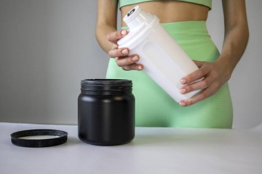 An athletic woman holds a prepared protein suplements or electrolytes for sport in a shaker bottle