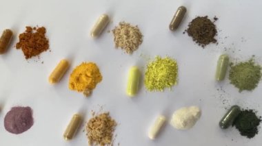 Opened and whole capsules of supplements on white background. Various pills and vitamins. From top right to left as follows: curcumin, vitamin C, ant tree bark, quercetin, q10, vegetable supplement