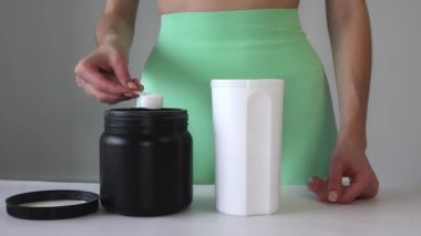 Close up of women with measuring scoop of whey protein and shaker bottle, preparing protein shake. A girl pours BCAA into a sports cup. The concept of sport, relaxation and muscle growth