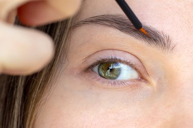 Eyebrow Serum for Women. An open-eyed girl applying a serum with essential oils and peptides to her eyebrows for strong growth, density and problem solving. Close-up