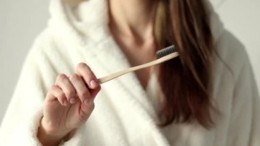 Environmentally friendly bamboo brush in a womans hand in close-up. A girl in a soft beige dressing gown.