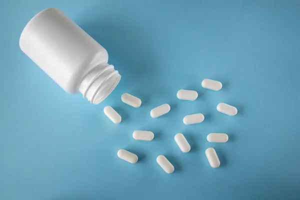 White pills and white jar on blue background, flat view from above. Pills for heart health. The concept of medicine and health care