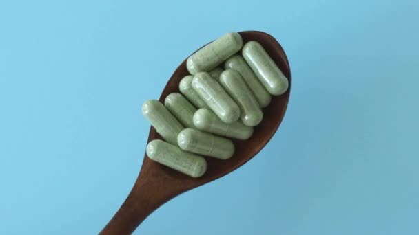 緑の健康サプリメント錠剤 ケールやビタグラスパウダーカプセル 青い背景に木製のスプーンで健康な腸のための食物繊維のプレバイオティクスサプリメント — ストック動画