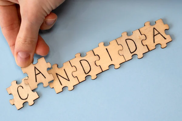 Candida is a word of wooden puzzles with letters, the concept of the parasitic fungus candida, blue background. Woman putting a puzzle together.