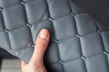 Woman holding a roll of gray quilted leather fabric, stitched with synthetic fabric. Fabric for furniture upholstery