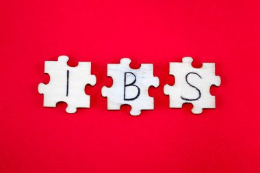 IBS Irritable Bowel Syndrome Acronym Written on Wooden Puzzles on a Red Background.