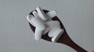 Magnesium Tablets. White tablets with rounded edges in wooden spoon on a beige background. Close-up