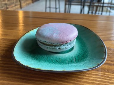 One pink and blue space-colored macaroons on a green plate on a table in a cafe