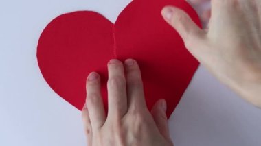 Womens hands glue a torn red paper heart together with Band-Aids. Unrecoverable, flawed.