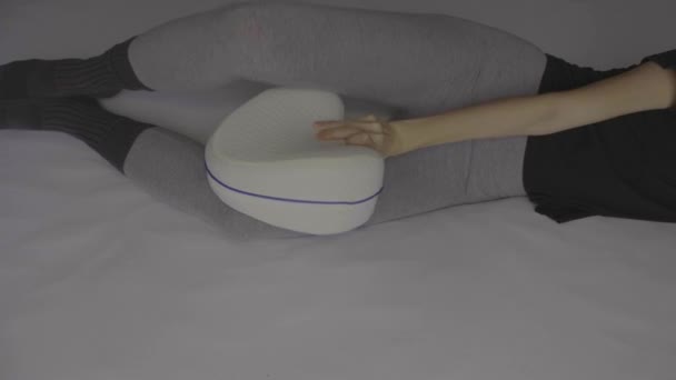 女人躺在床上 膝盖上抱着骨科枕头 — 图库视频影像