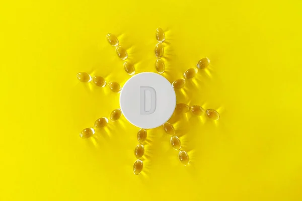 Sarı arka planda sarı ilaç kapsülü hapları ve sarı arka planda güneş şeklinde dizilmiş D vitamini içeren vatozlar var...