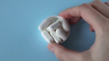 Magnesium Tablets. White tablets with rounded edges in a lid in a womans hand on a blue background