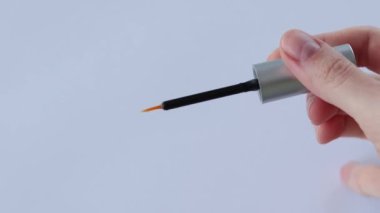Serum for growth and density of lashes with oils and peptides on a white background. Open tube with a thin brush in a womans hand
