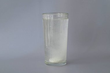 The fizzy round white tablet is dissolved in a glass of water. Supplement, vitamin C, calcium, D. Energy fitness drink