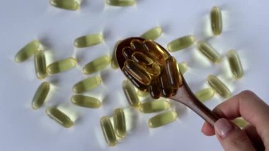 Wooden spoon with fish oil capsules, omega 3 on white background.
