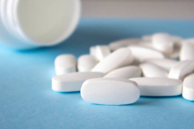 Mock-up of a white oval pill lying on the end on a blue background with a bunch of buds in the background and a jar. Selective focus, space for the name of the vitamin