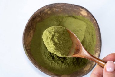 Green vitgrass powder in a bowl and wooden spoon on a white background. Ultimate Superfood for a Healthier You.