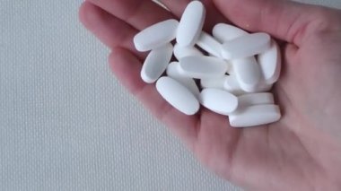 Kadınların elinde beyaz oval haplar, haplar, beyaz arka planda vitaminler var. Glutamin..