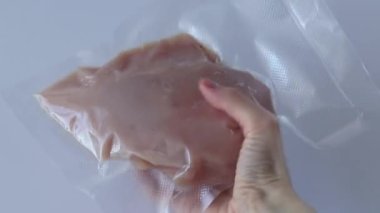 Vacuumed chicken breast, fillet on a white background in a womans hand. Preparation for boiling in sous vide