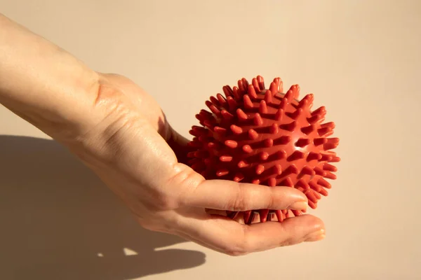 Spiked red rubber massage ball in a womans hand. Ball for recovery and rehabilitation or for relaxation and massage. Fitness equipment. Myofascial release concept