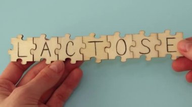 The word written on the wooden puzzles lettering is Lactose. A woman is putting a puzzle together