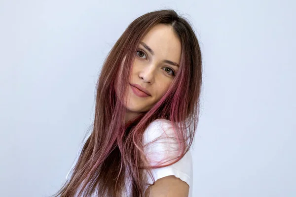 Portrait of a young woman in white with pink hair, head near shoulder. Girl on white background