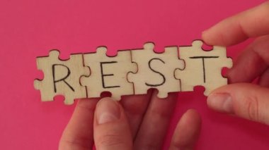 Rest inscription on assembled wooden puzzles in a womans hand on a red background
