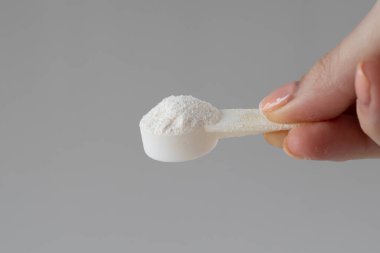 A measuring spoon with electrolyte powder and sports nutrition on a gray background in a womans hand.