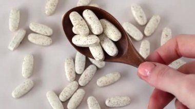 Bej arkaplanda benekler olan oval bej tabletlerle dolu bir tahta kaşık. Kompleks vitamin takviyesi. Yakın plan.