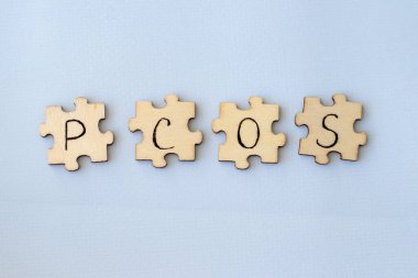 Polycystic Ovarian Syndrome. Hand Writing PCOS on wooden puzzles on a blue background.