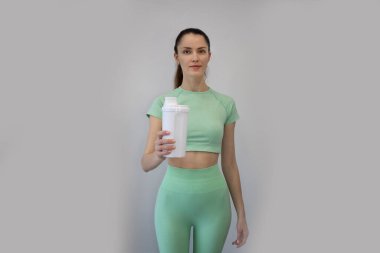 A slim young woman is holding a protein, amino acid sports shake for a workout