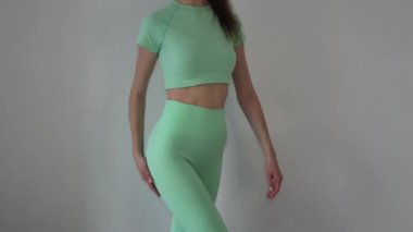 Slim young woman in a light turquoise tracksuit with leggings and a top.