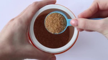 A jar with a measuring spoon of concentrated dry bone broth in a womans hand. Top view