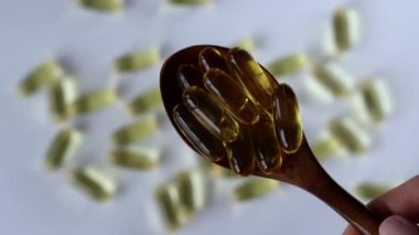 Wooden spoon with fish oil capsules, omega 3 on white background.