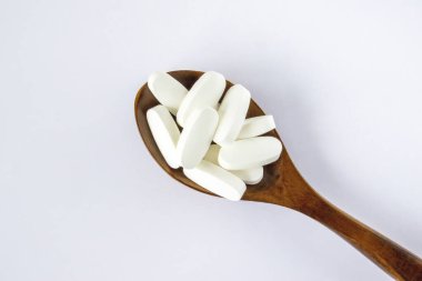 L glutamine white oval tabletsin a wooden spoon on a white background, top view