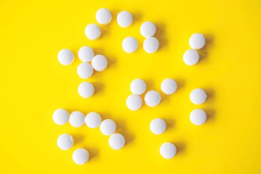 White round tablets on yellow background, top view.