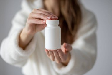 Woman is holding a white jar for tablets, pills, and supplements. Mock Up