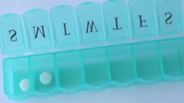 A woman fills a blue medical organizer with white tablets. Blue pill organizer for the week with open cells filled with one white round capsule each