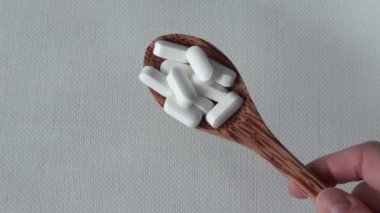 White tablets, supplements with rounded edges in a wooden spoon on a beige background in a womans hand