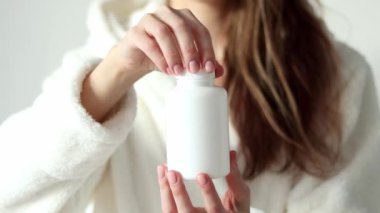 A woman opens the lid of a large white jar of pills. Mock Up.