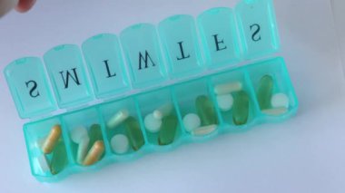 Pill organizer. Various capsules, vitamins and antibiotics in a plastic daily box. The woman fills the cells with tablets