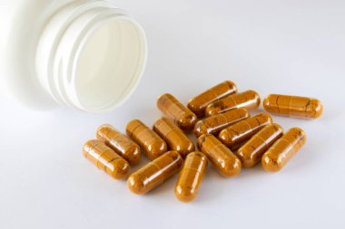 Vitamin curcumin, turmeric in capsules on a white background next to the lying jar of supplements. Pills and medications.