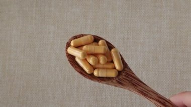 Coenzyme Q10 vitamin capsules in a wooden spoon on a beige background. Top view, copy space. Close-up