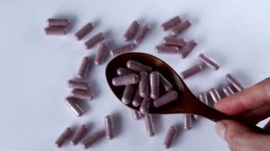 Pink capsules with supplements in a wooden spoon on a white background. Tablets and medicines. Vitamins, minerals, plant extracts and other useful substances. Tart Cherry.