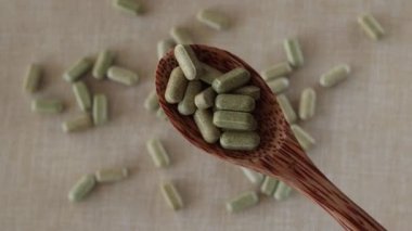 Vitamin from broccoli sulforaphane in capsules in a wooden spoon on a beige background. Tablets and medicines in green.
